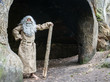 bearded hermit in a cave stands with stick in hand