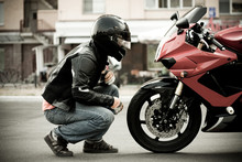 A Guy A Motorcyclist In A Helmet And A Leather Jacket And Jeans Sits Opposite A Motorcycle Of A Sports Red Color And Look Him Face To Face