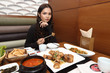 © Jade - Korea Food in Restaurant on wooden table, stir fried spicy pork with cheese on brass plate, girl fun eating sticky cheese, focus food blur woman