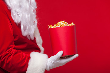 Christmas. Photo of Santa Claus gloved hand With a red bucket with popcorn, on a red background