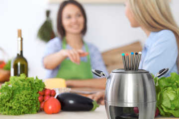 Fondue in a pot at the background of friends cooking together, close-up. Kitchen interiors and cookware