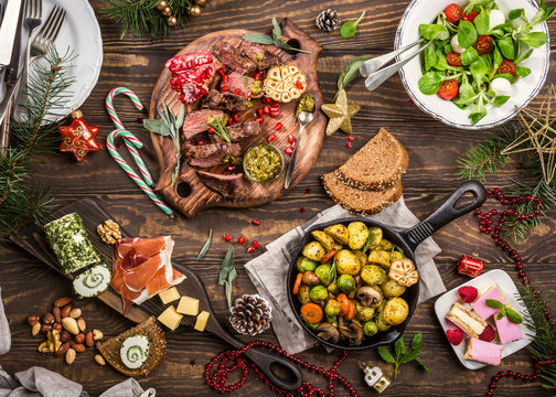 Flat lay of Delicious Christmas themed dinner table with roasted meat steak, appetizers and desserts. Top view. Holiday concept.