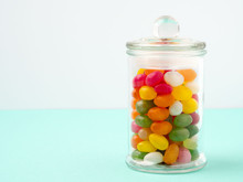 Glass Jar Filled With Candy And Caramel, With The Lid Closed On The Table. Turquoise Background With Empty Place For Text