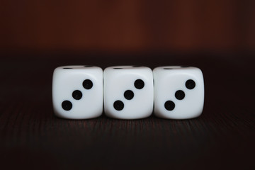 Wall Mural - Three white plastic dices in a row on brown wooden board background. Six sides cube with black dots. Number 333.