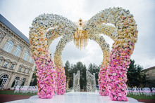 Wedding Altar Made Of Archs Of Pink, Yellow And White Flowers Stands On The Backyard