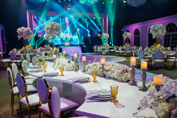 long dinner table decorated with white flowers, shiny candles and golden glasses stands in a beautif