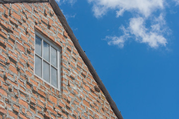 Window on brown brick wall and wooden roof in vintage style with blue sky background.