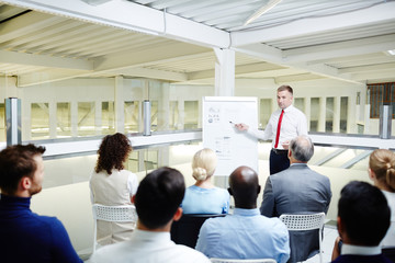 Canvas Print - Group of attendants listening to speaker and looking at data on whiteboard