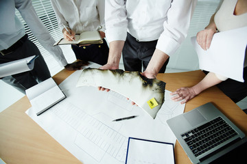 Members of aircraft accident board gathered together at open plan office and making assumptions concerning possible reasons of air crash, one of them holding plane wreckage in hands