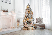 Classic White Christmas Interior With New Year Tree Decorated. Fireplace With Grey Chair, Clocks On The Wall And Presents Under The Tree