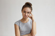 Thoughtful pensive young woman with hair bun making displeased grimace as if saying No, that's not an option while trying to solve problem, thinking over decision, holding head and looking sideways