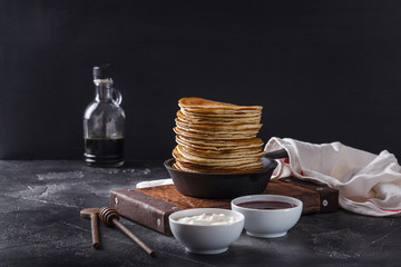 Pancakes with honey in a cast-iron frying pan on a black background, horizontal