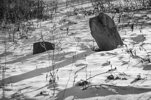 Zdjęcie XXL Czarno-biała fotografia dwóch nagrobków częściowo zasypanych śniegiem i podświetlonych cieniami.