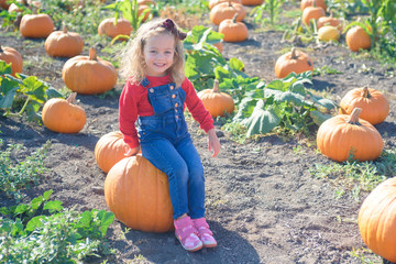 happy girl sitting on pumpkin at farm field patch