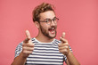 © wayhome.studio - Indoor shot of cheerful bearded man in spectacles and casual clothes indicates happily at you, chooses to compete, has positive expression. Handsome clever student makes choice, isolated on pink wall