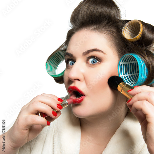 Fotomagnes Śmieszny portret błękitnooka kobieta w curlers robi makeup i patrzeje kamerę jak w lustrze nad białym tłem.
