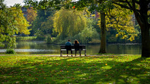 Couple Of Woman And Man Sitting On The Bench In Autumn Sunny Park