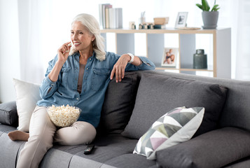 Glad senior woman watching tv at home