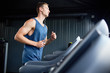 © Seventyfour - Side view portrait of muscular young man running on treadmill in modern gym during cardio workout, copy space