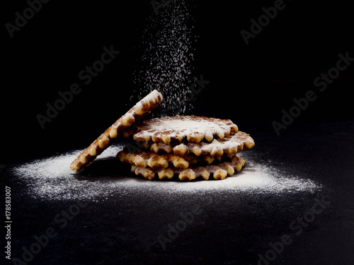 Fotografía White plate with homemade Belgian waffles, on top of poured sifting of powdered sugar on black background, very tasty snack