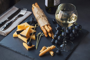 Wall Mural - Cheese plate served with crackers, grapes and glass of white wine on dark background.