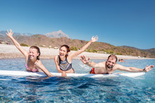 A Multinational Group Of Three Friends Of Students Laugh And Swim In The Sea With A Board Near The Beach. Concept Of Travel And Friendship