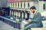 Fototapeta Nowy Jork - American Businessman with beard, mustache traveling, working in New York, wearing cadet blue suit, sitting outside office building, looking down, working on laptop computer. Instagram filtered effect