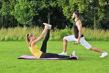 Wall Mural - Young sporty couple doing exercises in green park