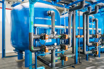 Large industrial water treatment and boiler room. Shiny steel metal pipes and blue pumps and valves.