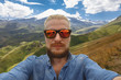 Young Traveler Man Makes Selfie On Background Of Mount Elbrus. Adventure Destionation Journey Concept