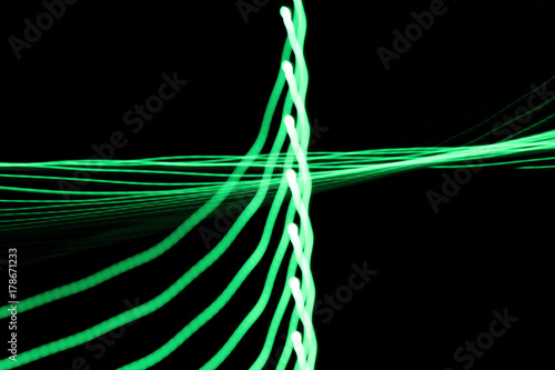 Green neon light lines and curves abstract image on black background due to came Poster