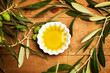 Aceite de Oliva en un cuenco blanco con hojas de oliva naturales sobre mesa de madera rústica. Vista superior y de cerca
