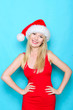 Happy blond girl with hands on hip. Wearing santa hat and red dress.