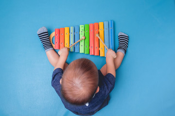 Bird eye view of Cute little Asian 18 months / 1 year old baby boy child hold sticks & plays a musical instrument colorful wooden toy xylophone