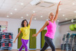 © undrey - Two young sporty women exercising in fitness studio, dancing, doing cardio, working on balance and coordination.
