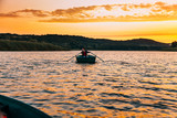 Fototapeta Krajobraz - Young man sailing boat on the river, sunset