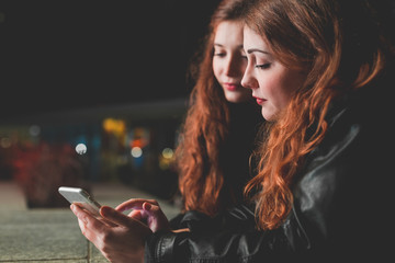 two young women outdoor city night using smart phone - internet, social network, technology concept