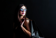 Elegant Brunette Woman Wears Sunglasses And Black Dress Holding Black Shopping Bags, Black Friday Concept