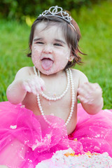 Wall Mural - Smiling happy baby toddler girl first birthday anniversary party. Laughing and sticking tongue out, face dirty from pink cake. Princess tiara costume