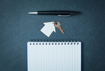 House and key with a pen and notepad on a blue background.