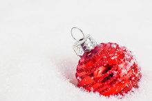 Close-up Of Red Xmas Ball Under Snowflakes In Snow. Christmas And New Year Concept With Copy Space. Christmas Greeting Card.