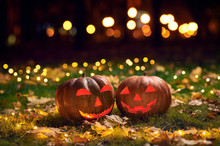 Two Smiling Halloween Pumpkins On A Grass With Lights In A Park At Night