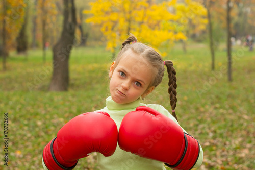 Zdjęcie XXL Mała dziewczynka w ogromnych rękawicach bokserskich robi złą twarz.