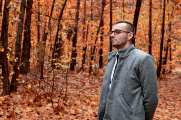 Modern handsome attractive man in gray coat in autumn forest. Fashion and clothing concept. Free place for text.