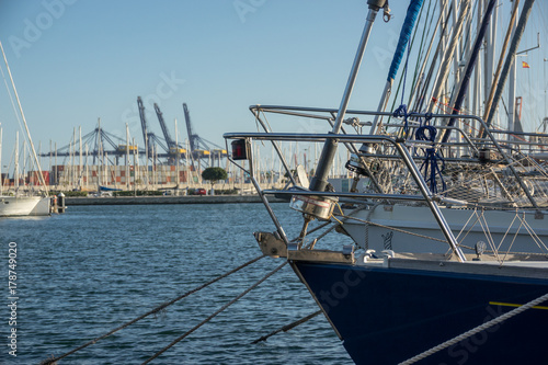 Fotografía prow of a sailboat, blurred background a commercial port with cargo containers