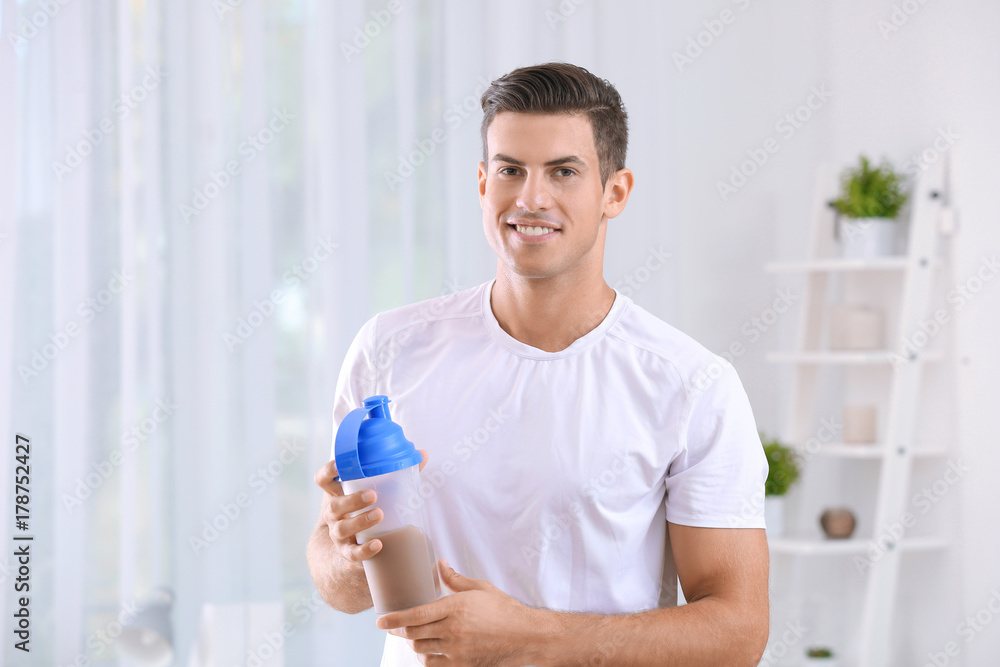 Young man holding bottle with protein shake indoors