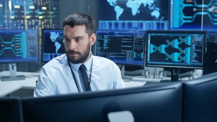 Fototapete - In the System Control Center Technical Operator Monitors Displays at His Workstation. He's Surrounded by Displays Showing Relevant Data. In the Background Data with Interactive Map.
