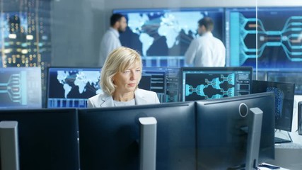 Fototapete - System Monitoring Room Professional Female Operator Observes Correct Functioning of the Facility. In the Background People Working with Interactive Map. Shot on RED EPIC-W 8K Helium Cinema Camera.