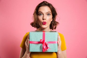 Wall Mural - Surprised brunette woman with bright makeup holding present, looking at camera