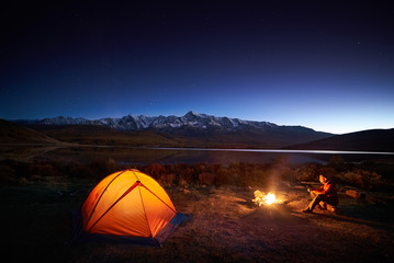 man tourists sitting in the illuminated tent near campfire